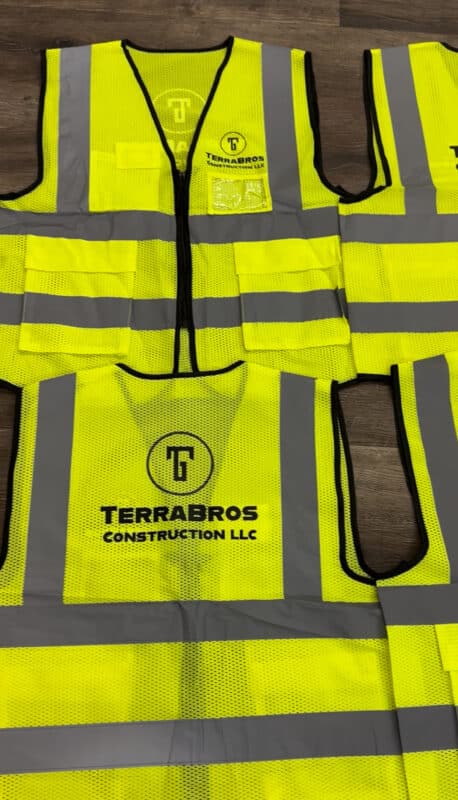 High-visibility yellow safety vests with reflective stripes and "Terrabros Construction LLC" branding displayed on a wooden surface.