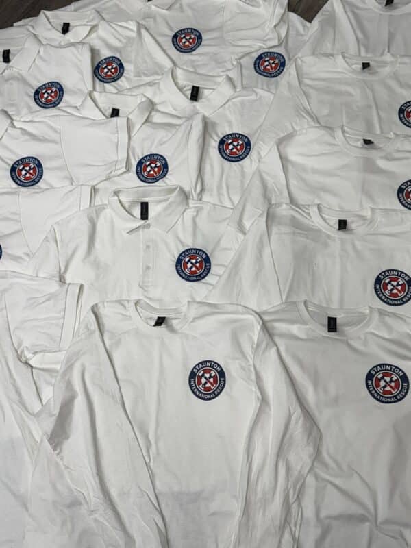 White shirts featuring a circular logo with "Staunton" text, arranged in a flat lay display, showcasing various styles including polo and long-sleeve options.