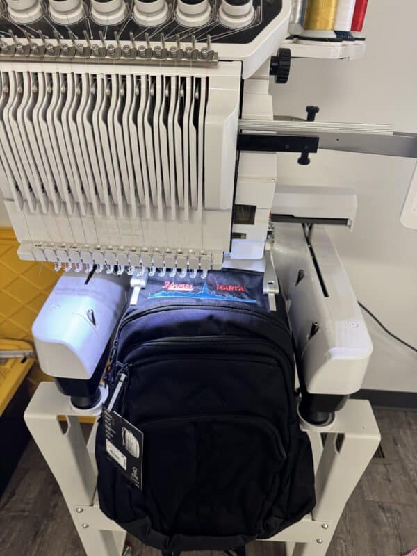 Embroidery machine working on a black backpack with visible stitching and tags, showcasing customization options for products at Embellishway.